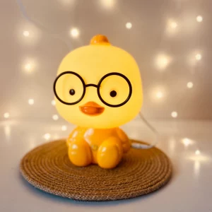 Kurczątko z okularami lampka nocna dziecięca LED, lampka nocna Kurczątko dziecięca, dla dzieci. Ładowanie przez USB sprawia, że jest praktyczna i wygodna. Bezpieczna dla dzieci, dostępna w kolorze żółtym.